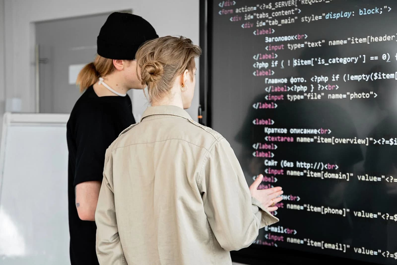 Two professionals reviewing source code on a large screen.