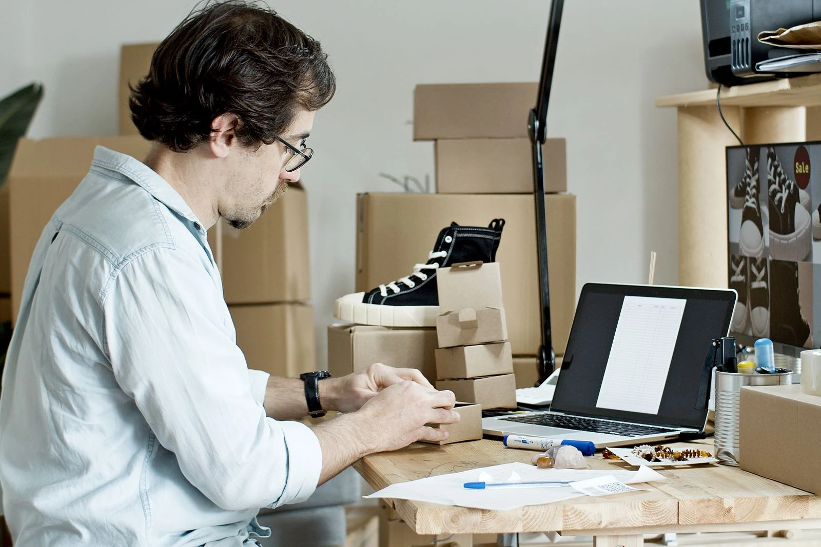 Una persona prepara un paquete junto a una computadora y al inventario de una tienda online.