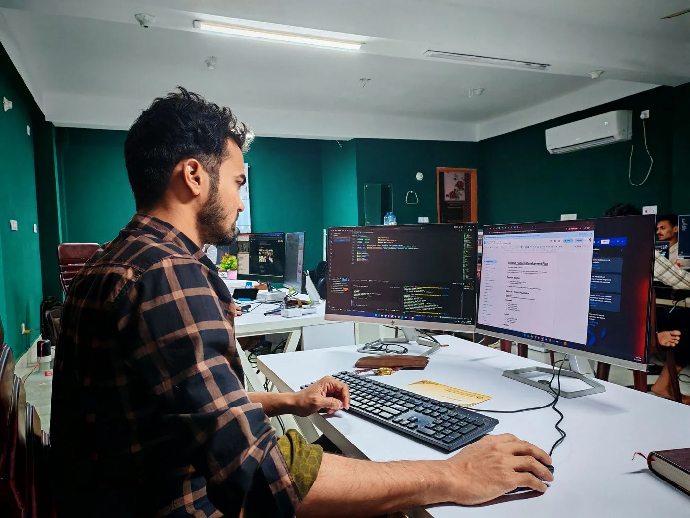 A software developer working with code on two monitors in an office.