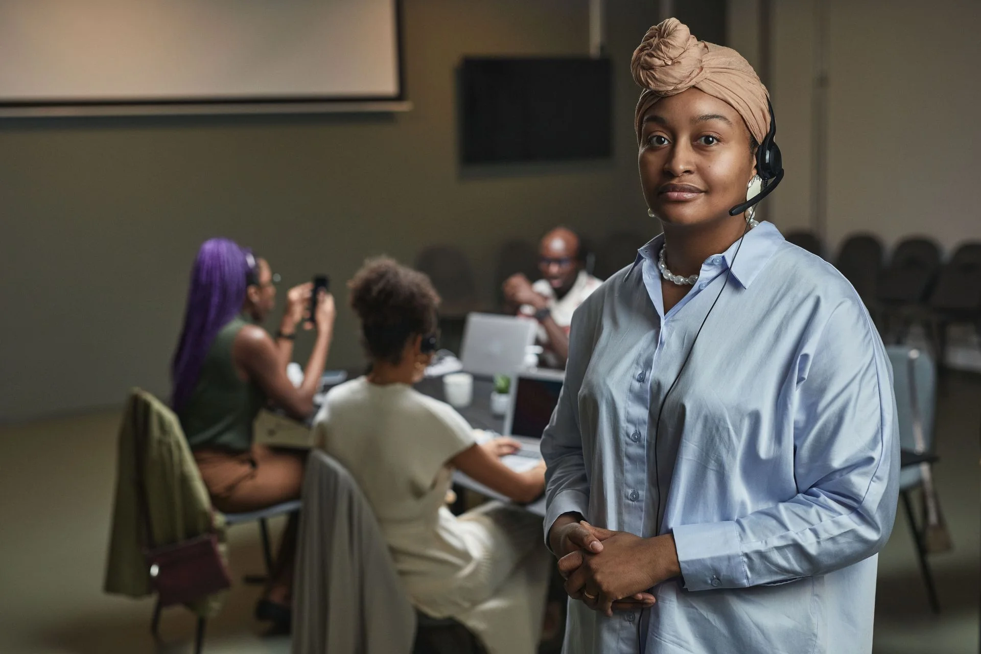 A professional wearing a headset beside a team in a work meeting.