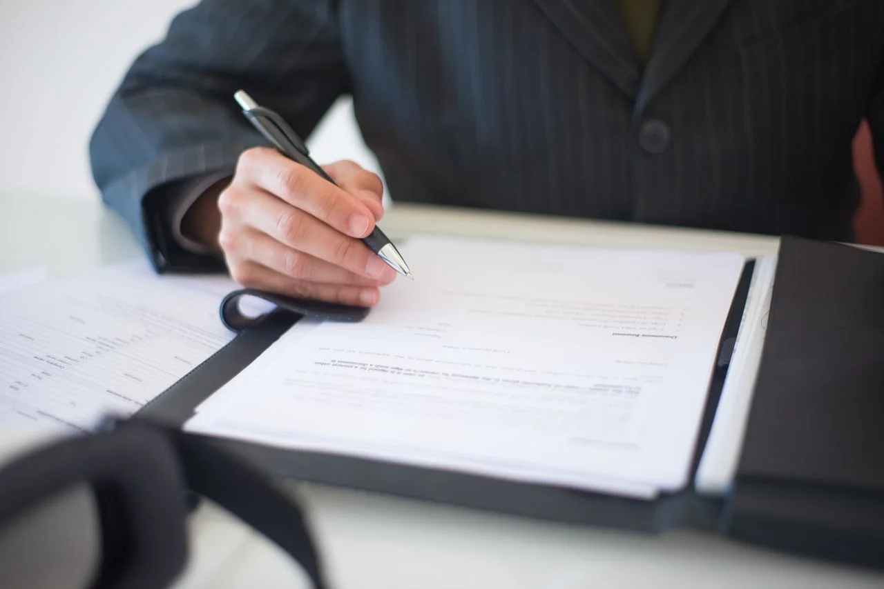 A person reviewing and signing documents in a folder on a desk.