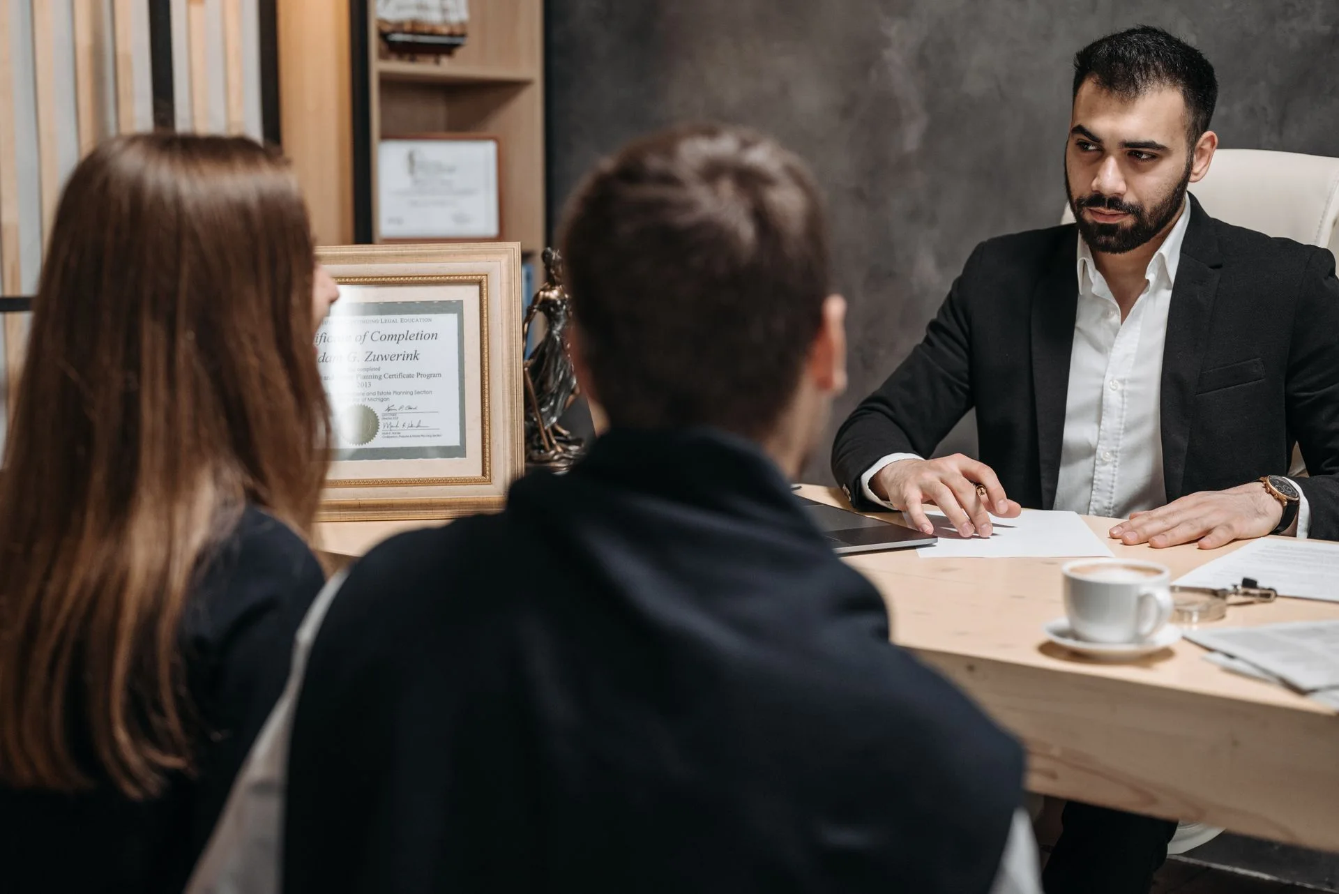 A professional reviews documents with two people during an office consultation.