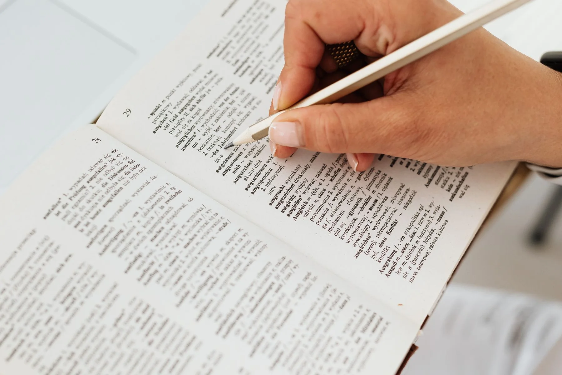 A person checks a dictionary entry with a pencil.